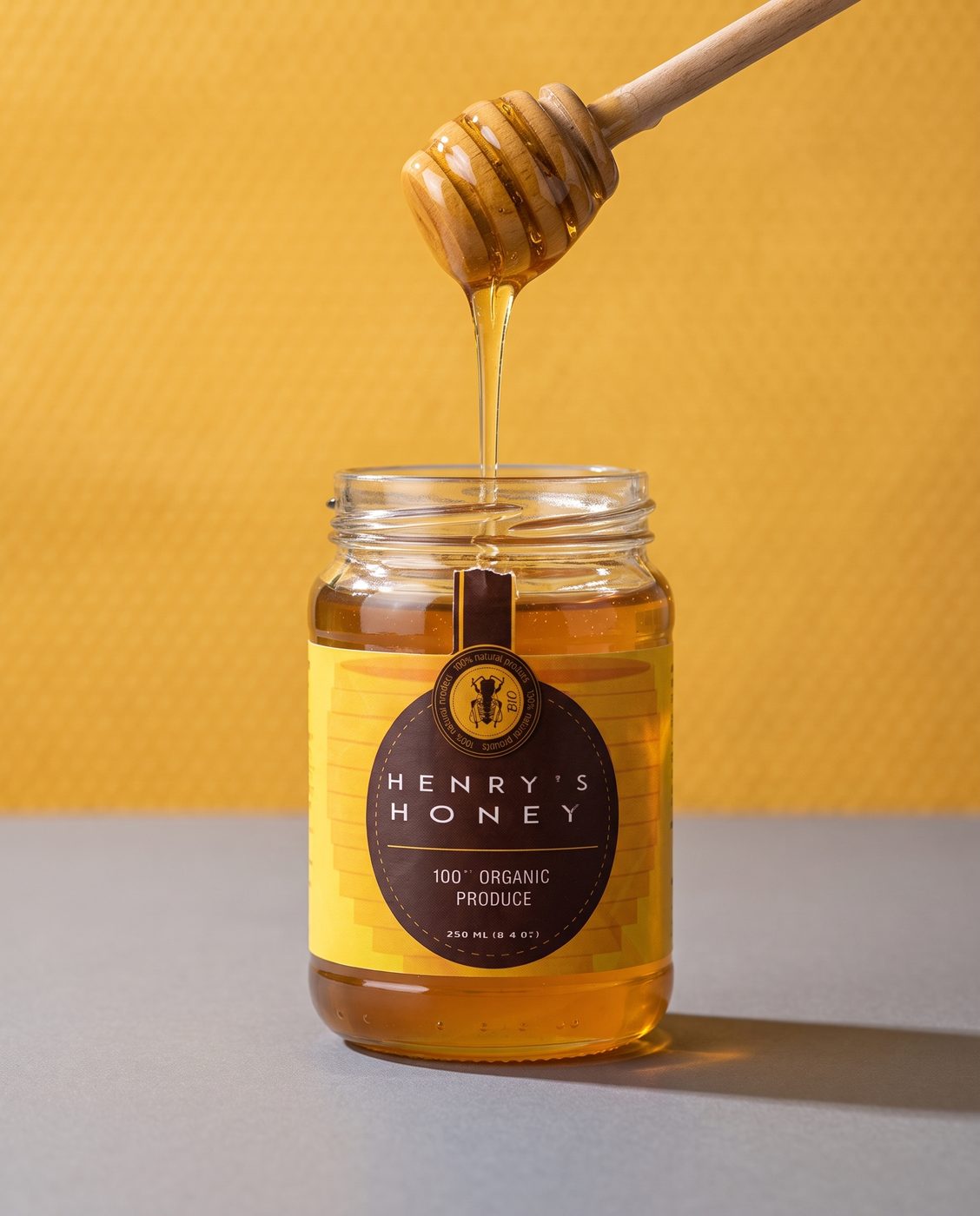 A jar of Henry's Honey with a dipper dripping into it, on a mustard ground